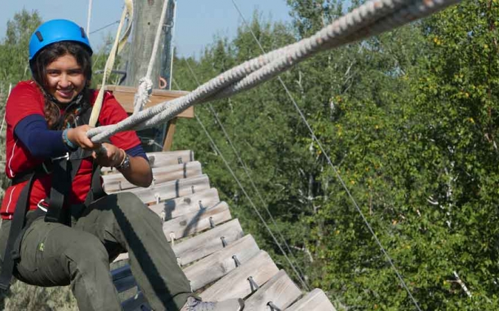 a students holds onto a rope while completing a ropes course with outward bound